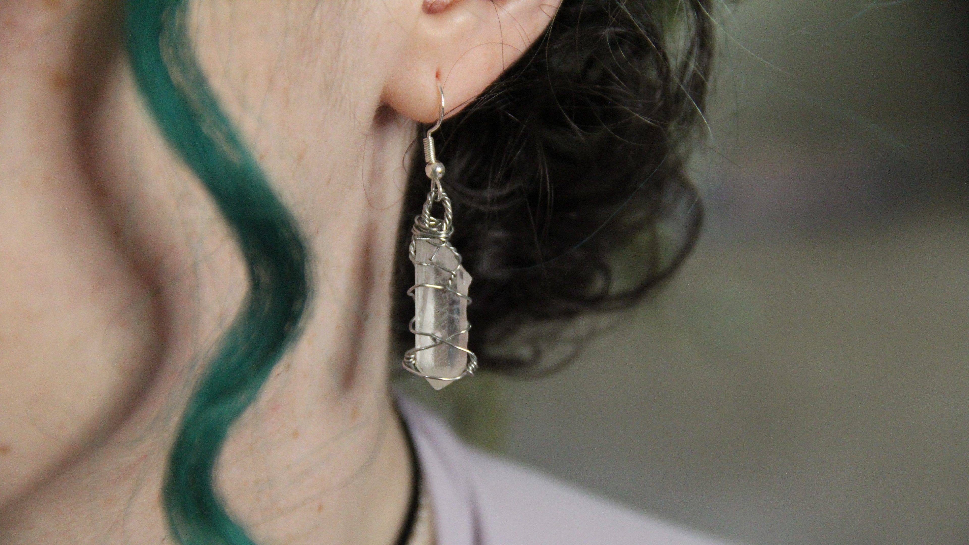 Close-up of a person wearing a crystal earring with green hair.